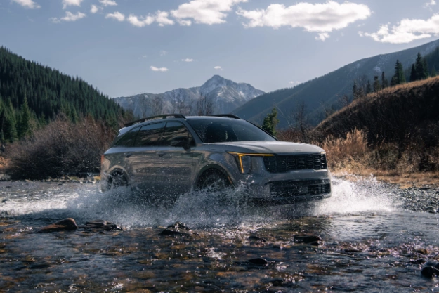 2024 Kia Sorento in brown, three-quarter front view, driving through a river of water in the mountains