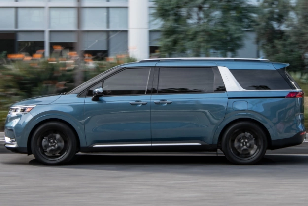 2024 Kia Carnival Driving Past A Large Building Side-View 