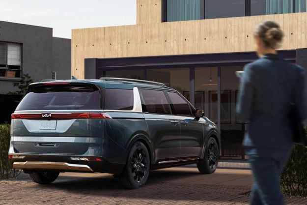 2024 Kia Carnival Parked In Front Of A Residential Building While The Owner Walks Towards The Vehicle Three-Quarter View 