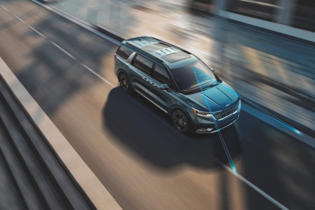 2024 Kia Carnival Driving Fast Through City Roads Top Three-Quarter View 