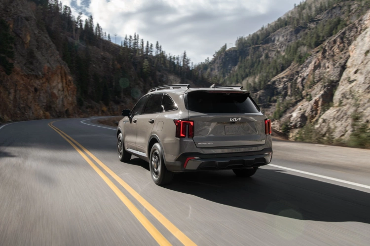 2024 Kia Sorento in brown, three-quarter back view, driving through a winding road in the mountains